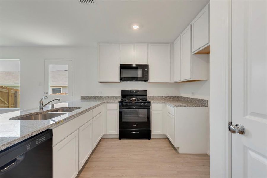 Kitchen with light wood-type flooring, white cabinets, black appliances, light stone countertops, and sink