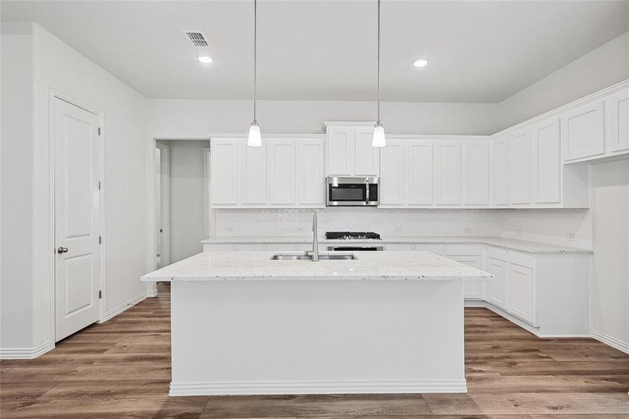 Kitchen with white cabinetry, light wood-type flooring, an island with sink, light stone countertops, and sink