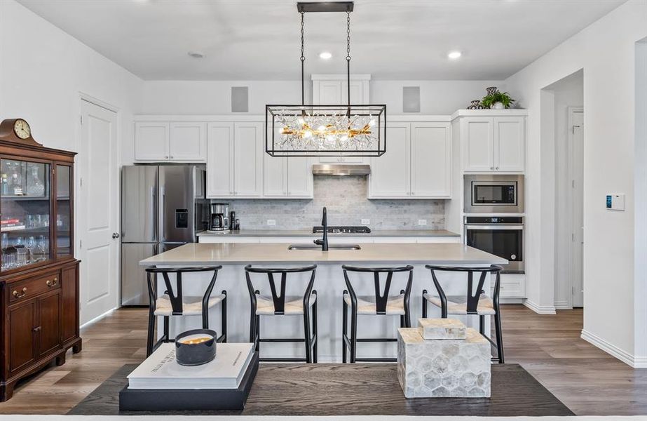 Kitchen with decorative light fixtures, an island with sink, appliances with stainless steel finishes, and white cabinetry