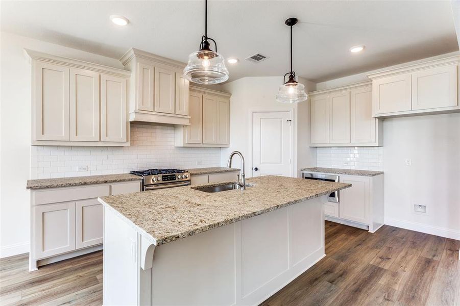 Kitchen featuring backsplash, pendant lighting, hardwood / wood-style flooring, gas stove, and sink