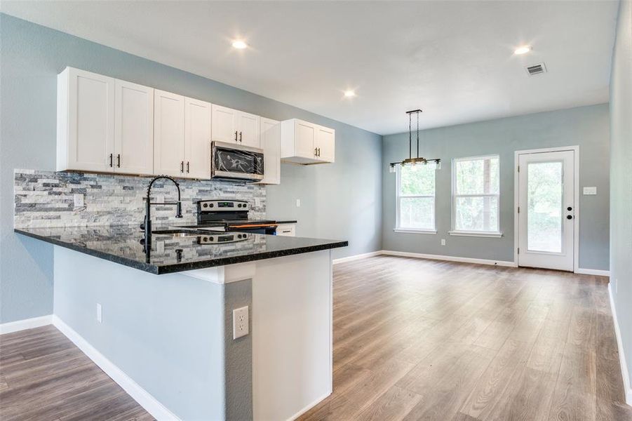 Kitchen featuring dark stone counters, stainless steel appliances, kitchen peninsula, backsplash, and light hardwood / wood-style floors