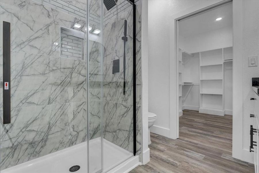 Bathroom featuring wood-type flooring, toilet, and a shower with door