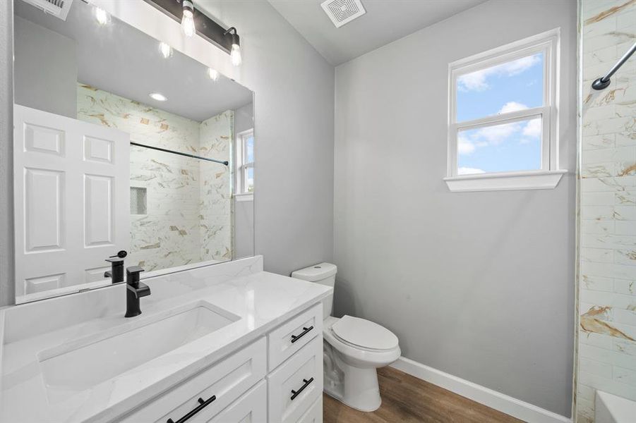 Full bathroom with vanity, toilet, tiled shower / bath, and hardwood / wood-style floors