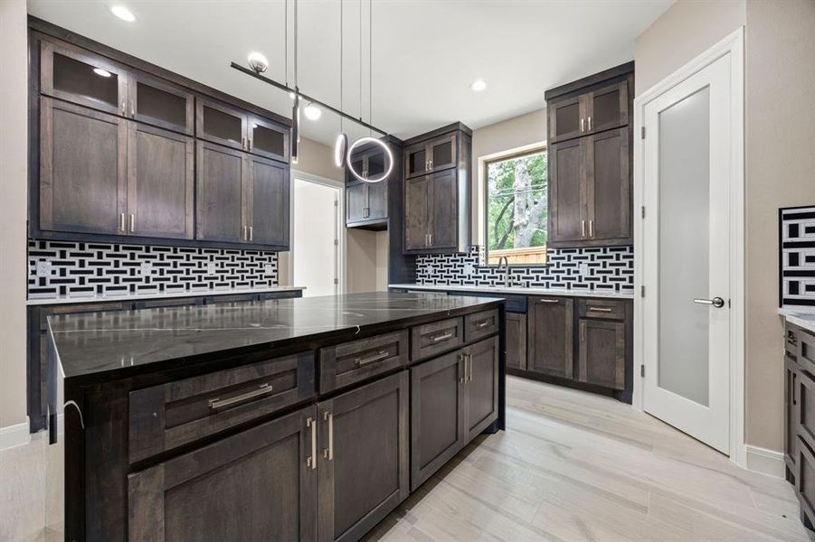 Kitchen with pendant lighting, decorative backsplash, dark brown cabinetry, dark stone countertops, and a kitchen island