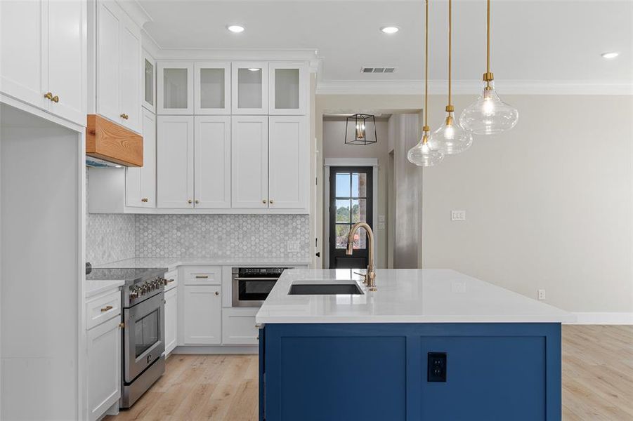 Kitchen featuring appliances with stainless steel finishes, hanging light fixtures, a kitchen island with sink, and white cabinets