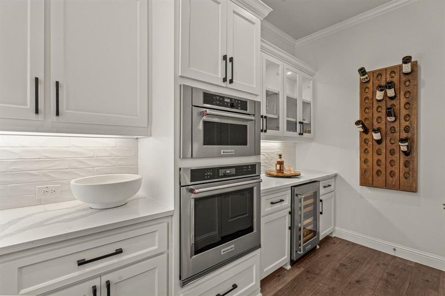 Kitchen with double oven, dark wood-type flooring, backsplash, wine cooler, and white cabinets