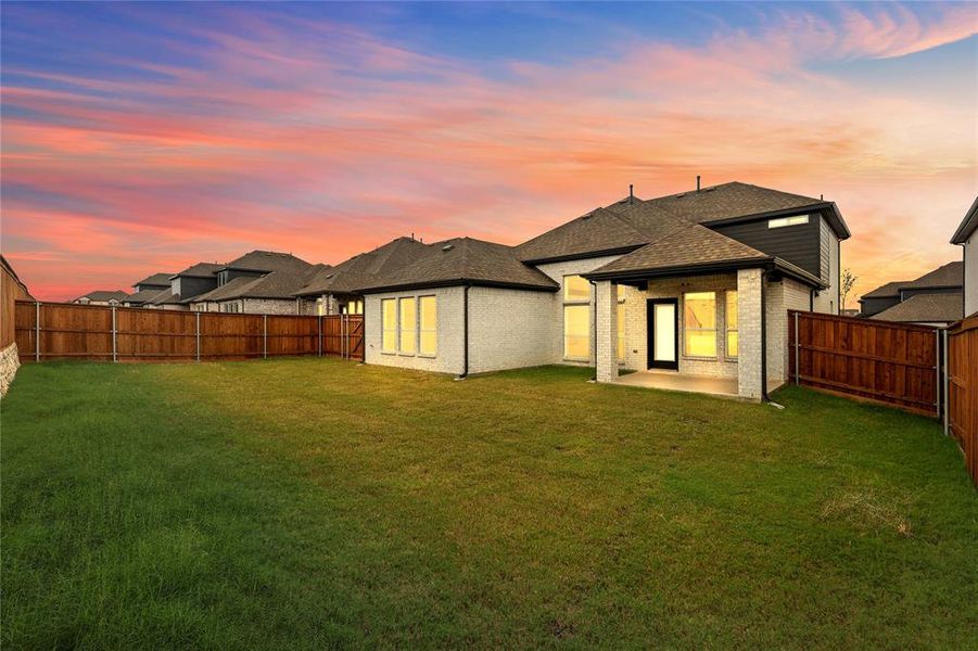 Back house at dusk with a yard and a patio