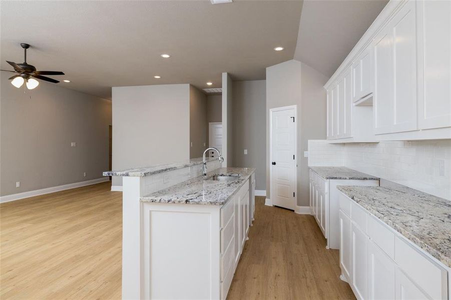 Kitchen featuring tasteful backsplash, ceiling fan, light hardwood / wood-style floors, sink, and a center island with sink