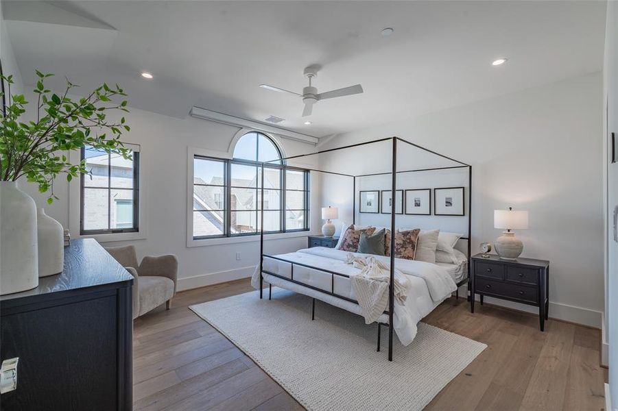 Primary bedroom featuring ceiling fan and light hardwood flooring, Pella windows, and automatic shades