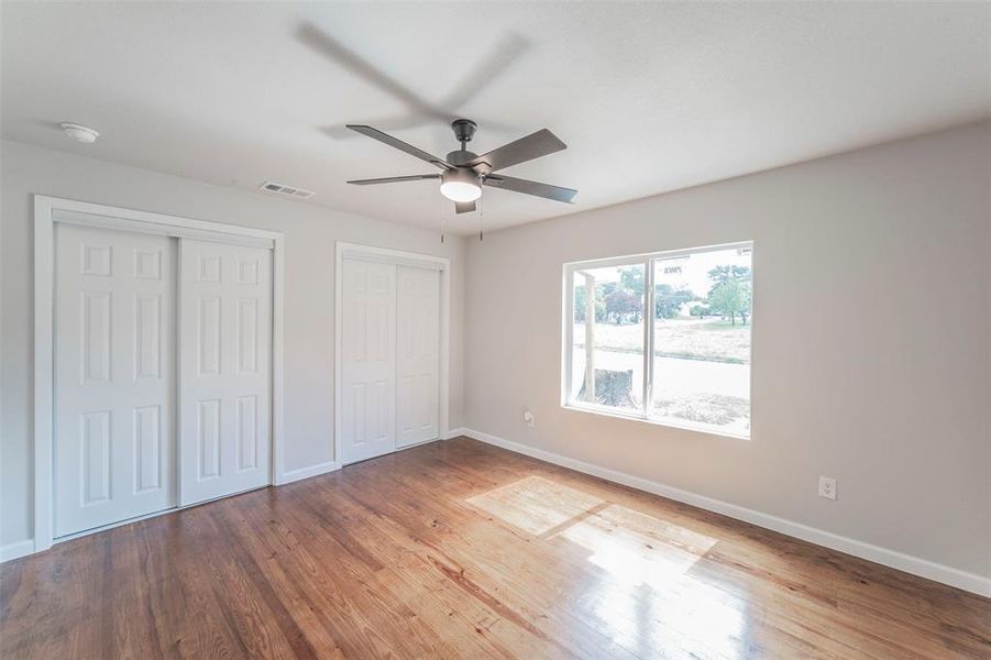 Primary bedroom with ceiling fan, hardwood / wood-style floors, and multiple closets