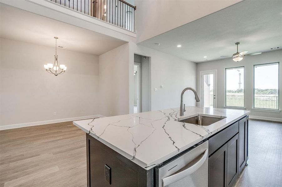 Kitchen featuring light stone counters, sink, stainless steel dishwasher, light hardwood / wood-style flooring, and ceiling fan with notable chandelier