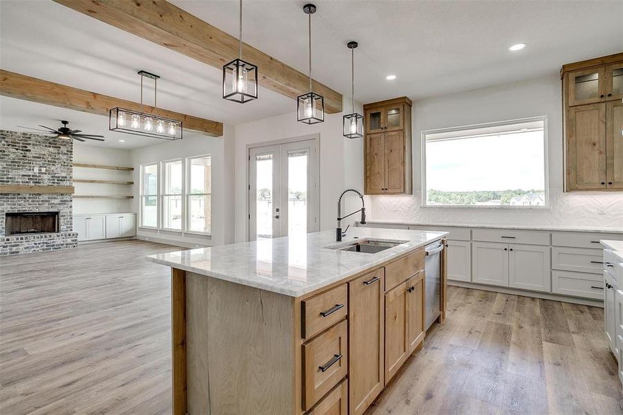 Kitchen with a fireplace, sink, ceiling fan, beam ceiling, and a kitchen island with sink