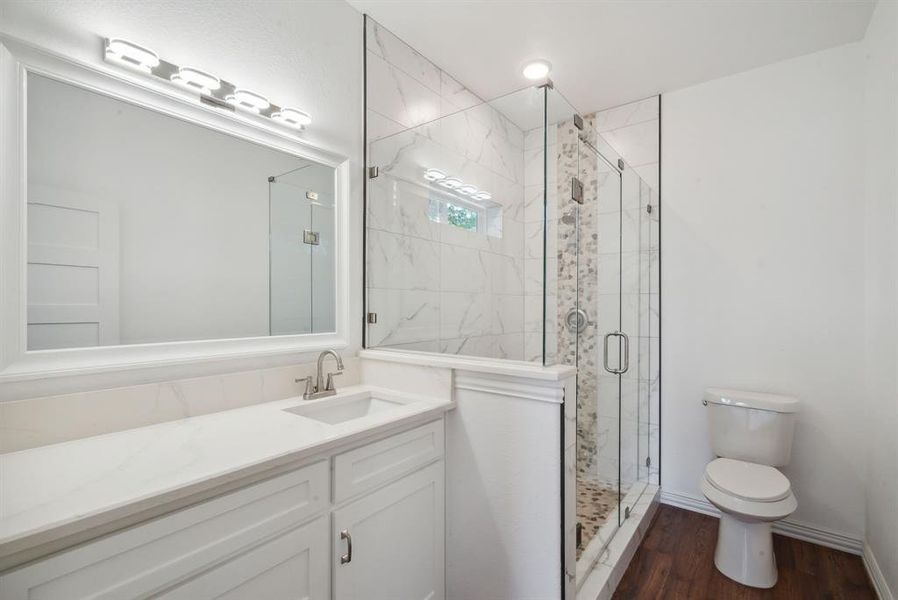 Bathroom with hardwood / wood-style floors, vanity, toilet, and an enclosed shower