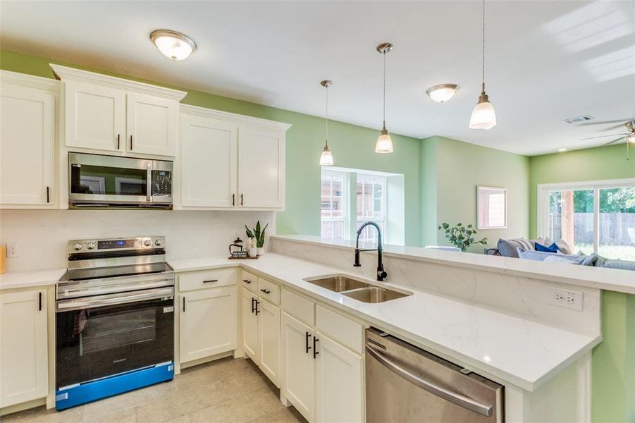 Kitchen with decorative light fixtures, appliances with stainless steel finishes, sink, and kitchen peninsula