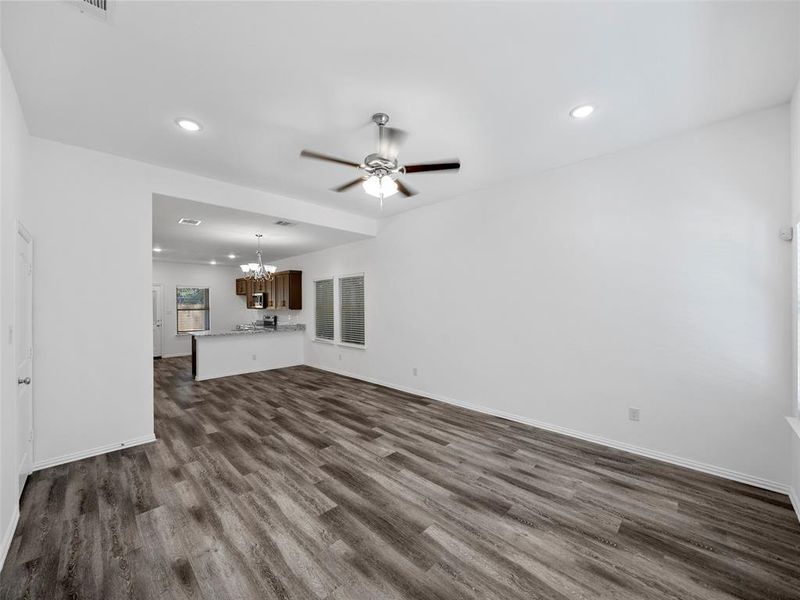 Unfurnished living room featuring dark wood-type flooring and ceiling fan with notable chandelier