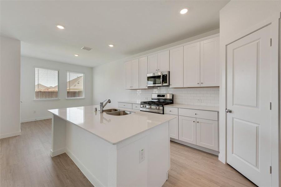 Kitchen with an island with sink, sink, stainless steel appliances, and white cabinets