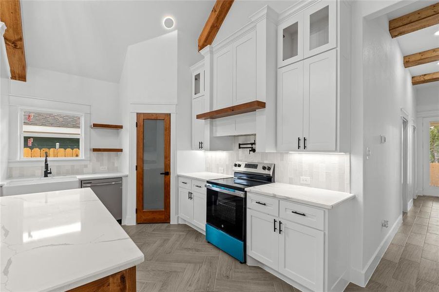 Kitchen with white cabinetry, light stone countertops, appliances with stainless steel finishes, and vaulted ceiling with beams