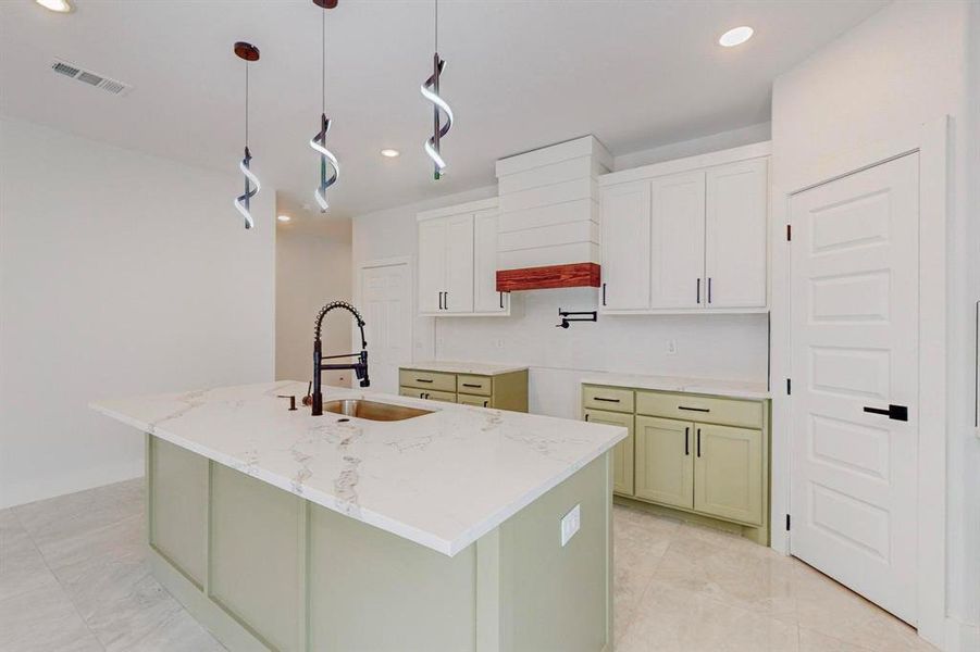 Kitchen with light tile patterned flooring, sink, decorative light fixtures, and an island with sink