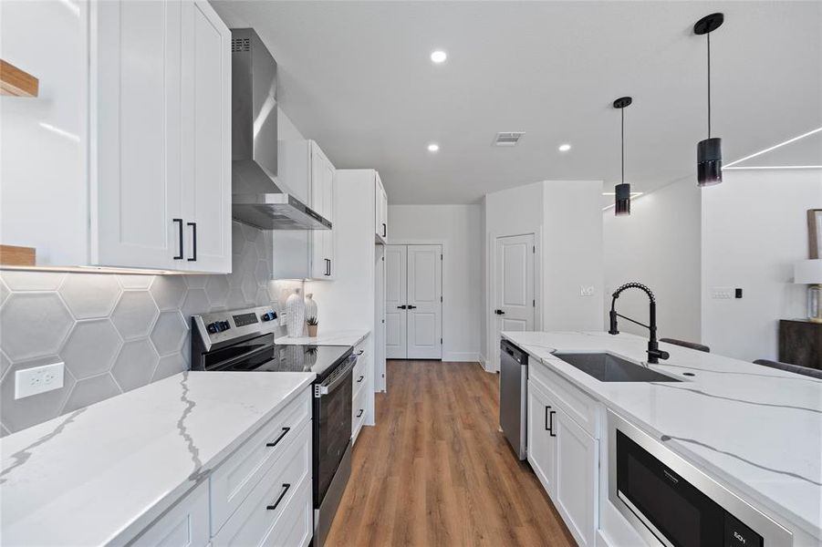 Kitchen featuring wall chimney range hood, sink, stainless steel appliances, hanging light fixtures, and white cabinetry