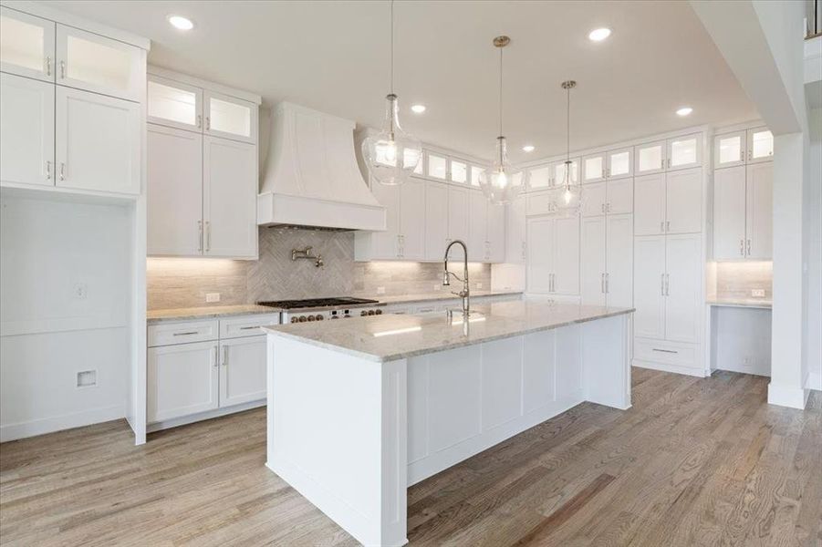 Kitchen featuring premium range hood, tasteful backsplash, light wood-type flooring, and white cabinetry
