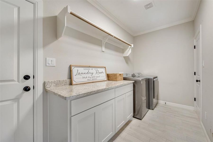 Laundry room featuring cabinets, light hardwood / wood-style floors, ornamental molding, and washing machine and dryer