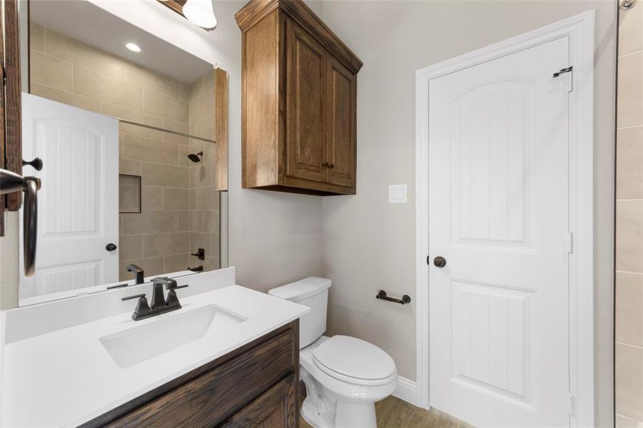 Bathroom featuring toilet, hardwood / wood-style flooring, vanity, and tiled shower