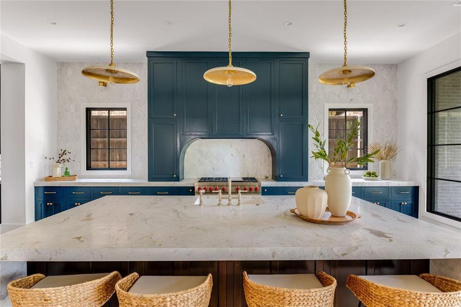 Kitchen featuring an island with sink, blue cabinetry, decorative light fixtures, and sink