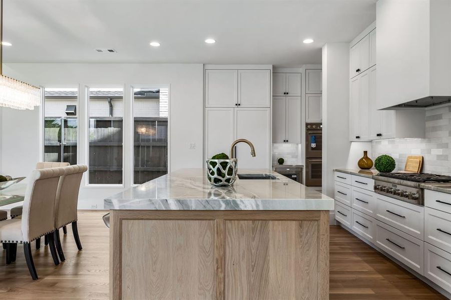 Kitchen with premium range hood, hardwood / wood-style floors, decorative backsplash, and an island with sink