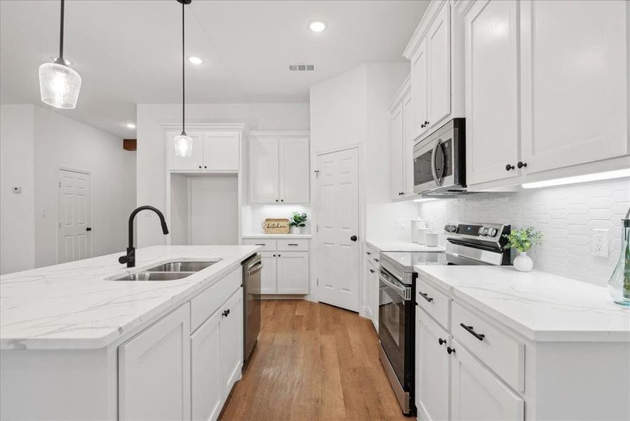 Kitchen featuring light wood-type flooring, appliances with stainless steel finishes, white cabinetry, sink, and an island with sink