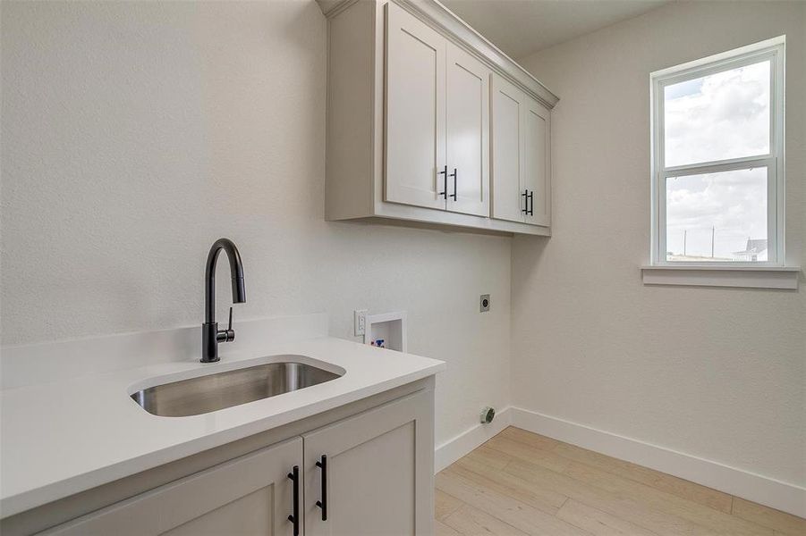 Laundry area with sink, cabinets, a healthy amount of sunlight, and light wood-type flooring