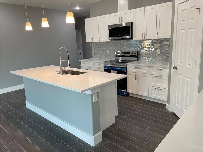 Kitchen featuring tasteful backsplash, sink, stainless steel appliances, decorative light fixtures, and white cabinets