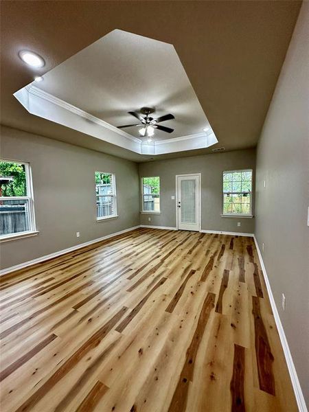 Unfurnished living room with a skylight, a raised ceiling, light hardwood / wood-style flooring, and ceiling fan