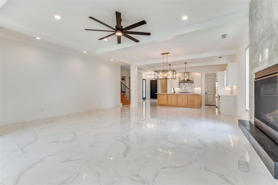 Unfurnished living room featuring light tile floors and ceiling fan with notable chandelier