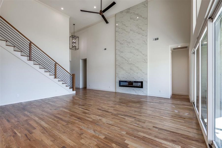 Unfurnished living room with a towering ceiling, light hardwood / wood-style floors, a fireplace, and crown molding