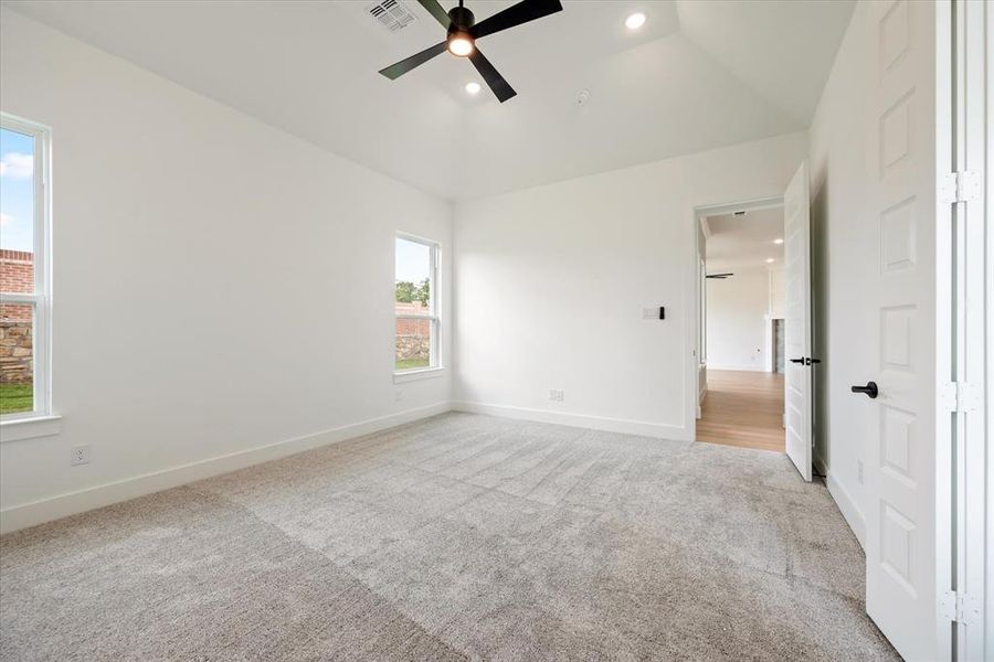 Unfurnished bedroom featuring light carpet, multiple windows, ceiling fan, and vaulted ceiling