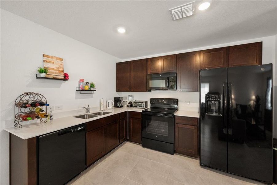 Kitchen with dark brown cabinets, black appliances, sink, and light tile patterned floors