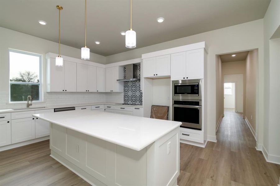 Kitchen featuring appliances with stainless steel finishes, wall chimney range hood, tasteful backsplash, and white cabinetry