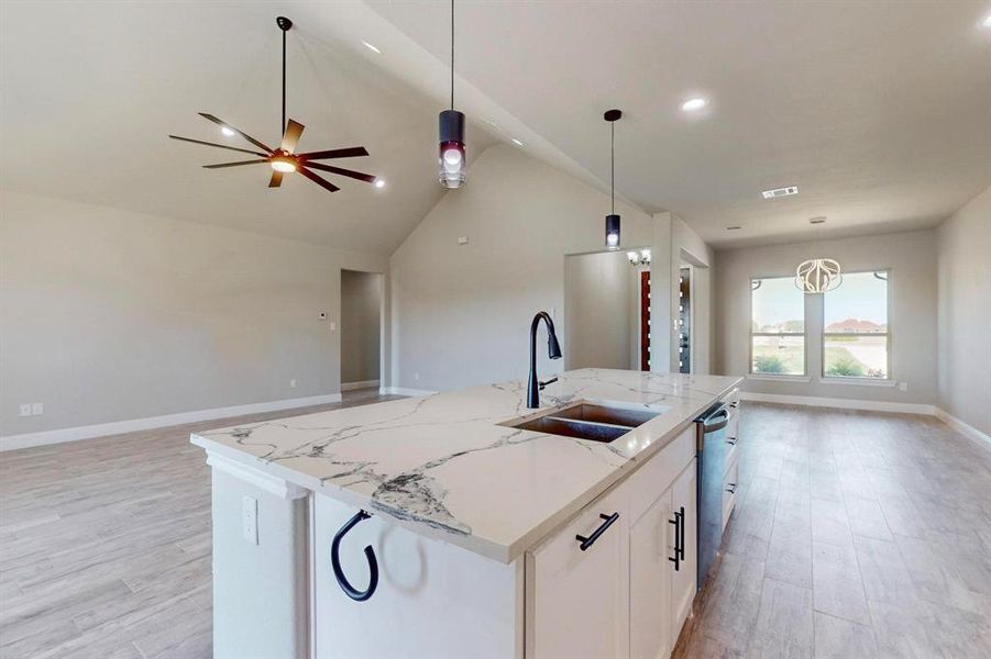 Kitchen featuring ceiling fan, light wood-type flooring, a center island with sink, and hanging light fixtures