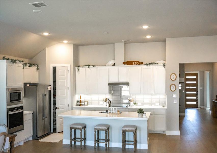 Kitchen with an island with sink, white cabinets, vaulted ceiling, a kitchen bar, and stainless steel appliances