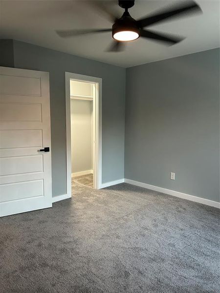 Unfurnished bedroom with ceiling fan, dark colored carpet, a spacious closet, and a closet