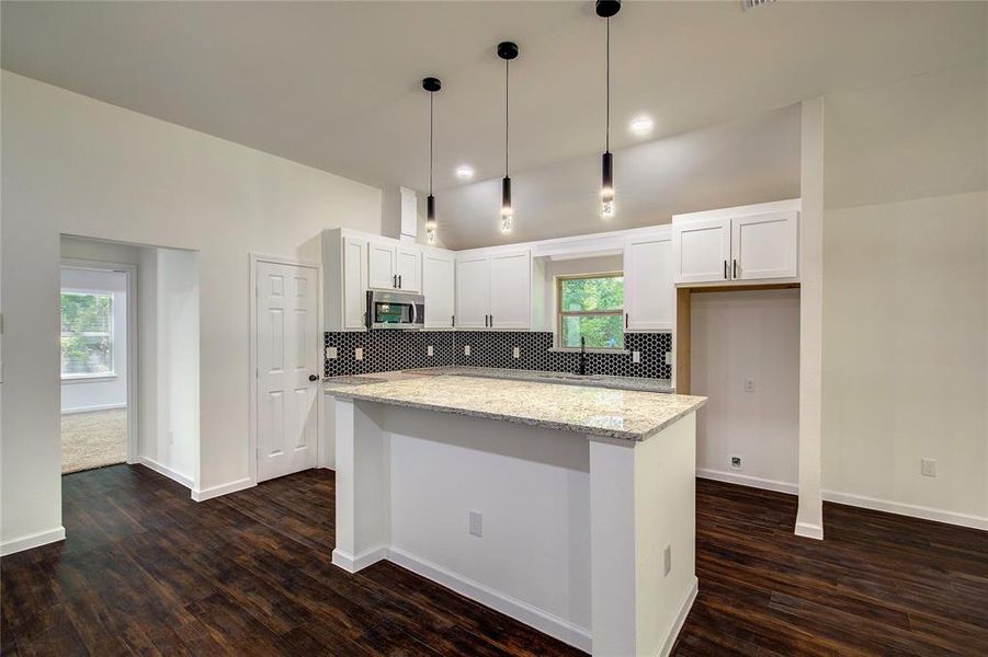 Kitchen with light stone countertops, tasteful backsplash, pendant lighting, dark hardwood / wood-style flooring, and white cabinets