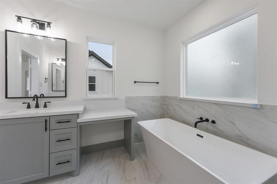 This is a modern primary bathroom featuring a double vanity with framed black matted mirrors, ample storage space and a spacious bathtub with a marble surround. The room is well-lit, with a frosted window ensuring privacy.