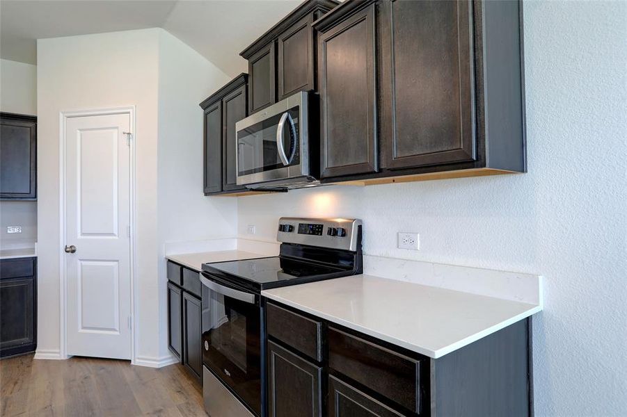 Kitchen featuring dark brown cabinets, light hardwood / wood-style floors, lofted ceiling, and stainless steel appliances