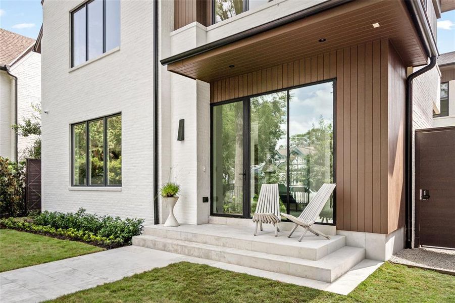 The welcoming porch showcases a modern slurried brick exterior with sleek black window frames, complemented by rich, treated pine ceilings and Moroccan limestone flooring on the steps and patio.