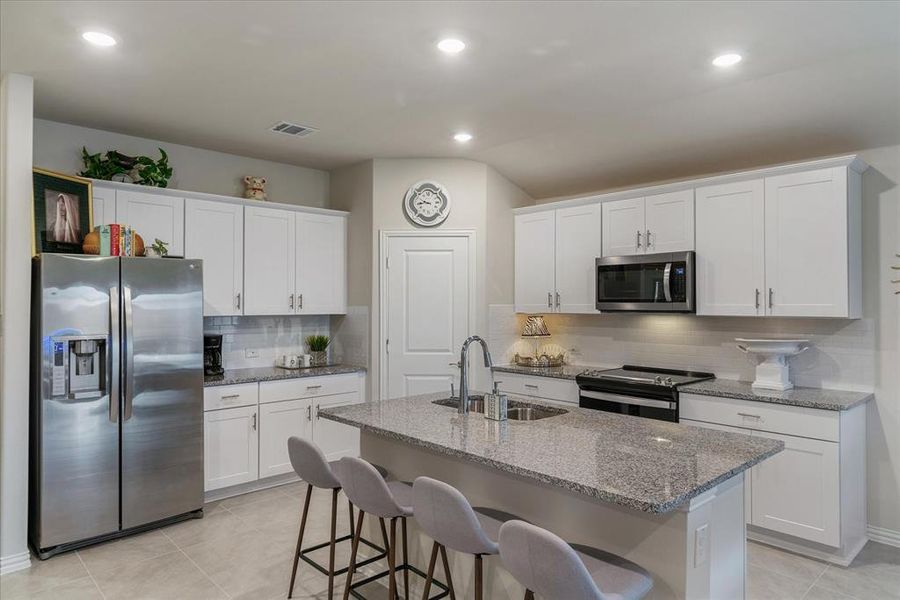 Kitchen with light stone counters, stainless steel appliances, white cabinetry, and walk in pantry.