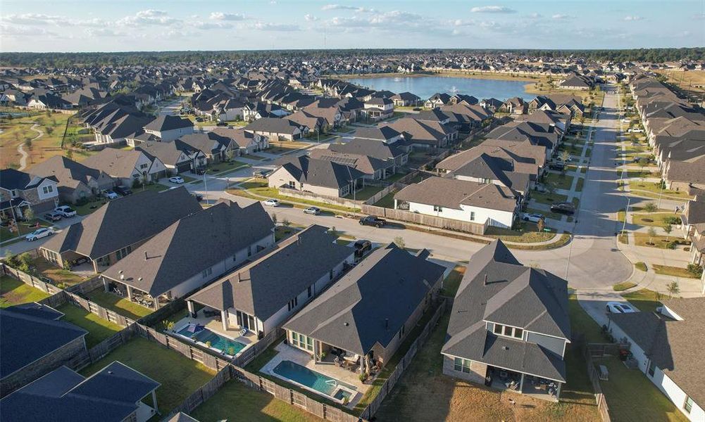 This aerial photo showcases a modern suburban neighborhood with well-ordered single-family homes, some featuring backyard pools. The community is situated near a large body of water, offering a scenic environment. Roads are neatly laid out for easy access.