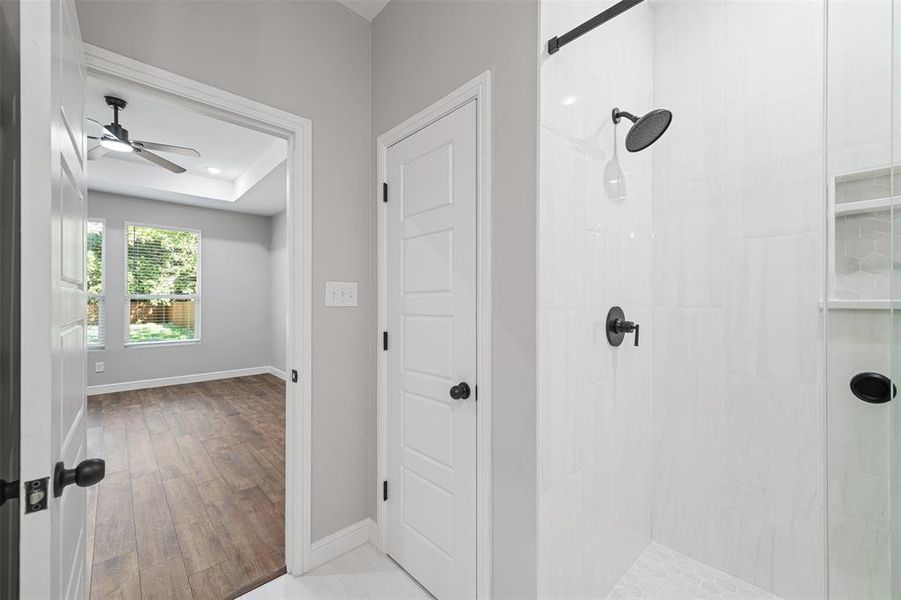 Bathroom featuring a raised ceiling, ceiling fan, wood-type flooring, and a tile shower