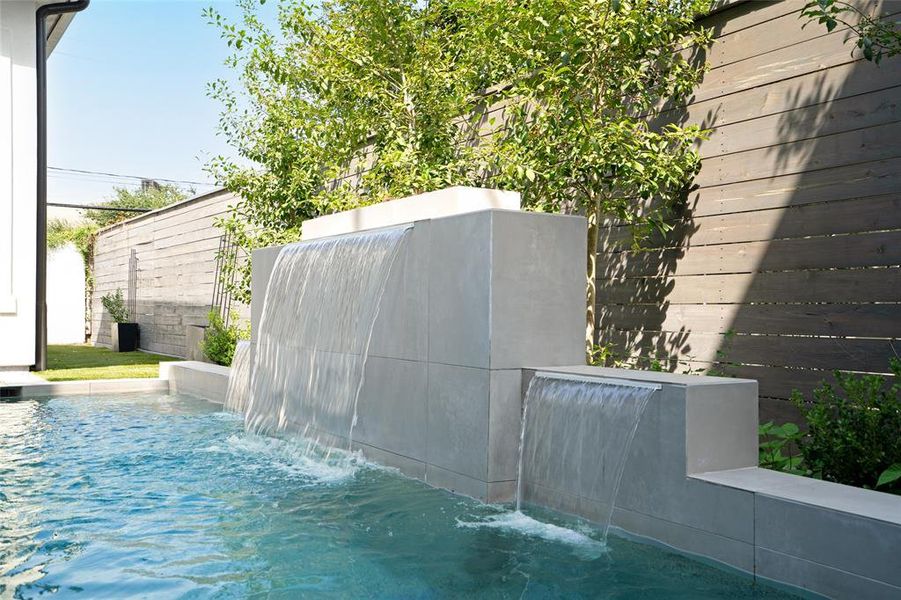 This stunning outdoor feature combines the warmth of a firepit with the soothing ambiance of a cascading waterfall. Positioned at the top of a sleek, contemporary wall, the firepit adds an element of luxury and comfort to the space. Below, a modern waterfall flows seamlessly into the pool, creating a tranquil retreat.