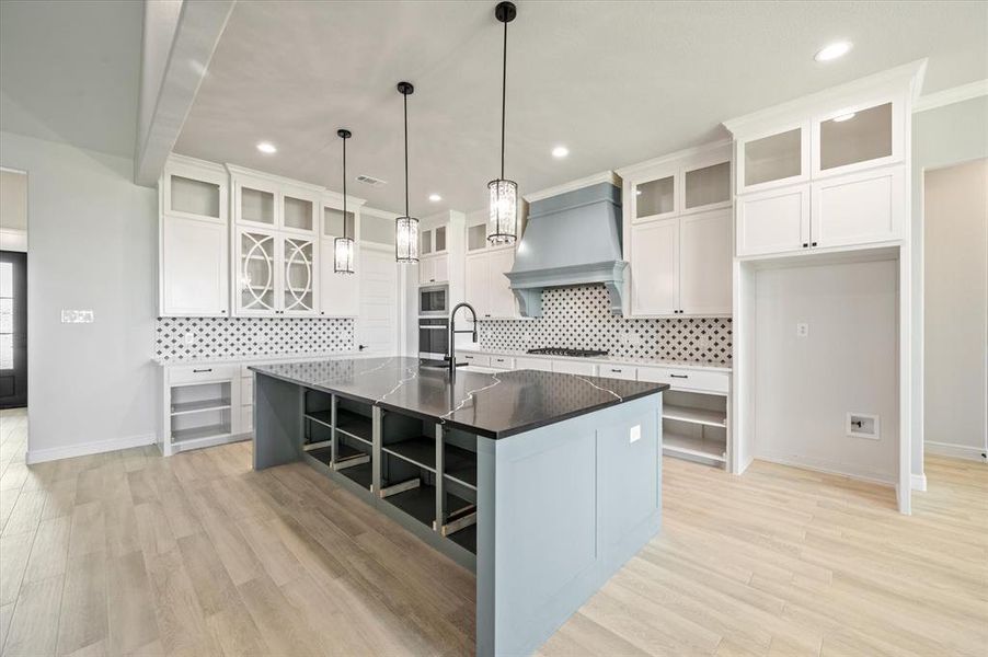 Kitchen with white cabinetry, light hardwood / wood-style flooring, a center island with sink, and custom range hood