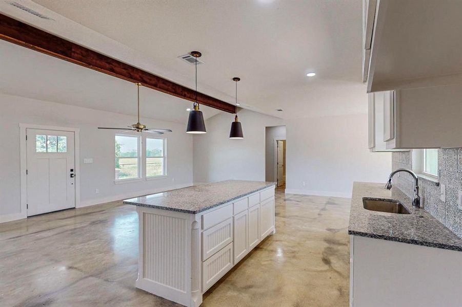 Kitchen featuring white cabinets, sink, hanging light fixtures, stone countertops, and beam ceiling